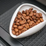 A young boy tamping coffee grounds with a wooden tamper while observing a digital scale in a bright café setting.