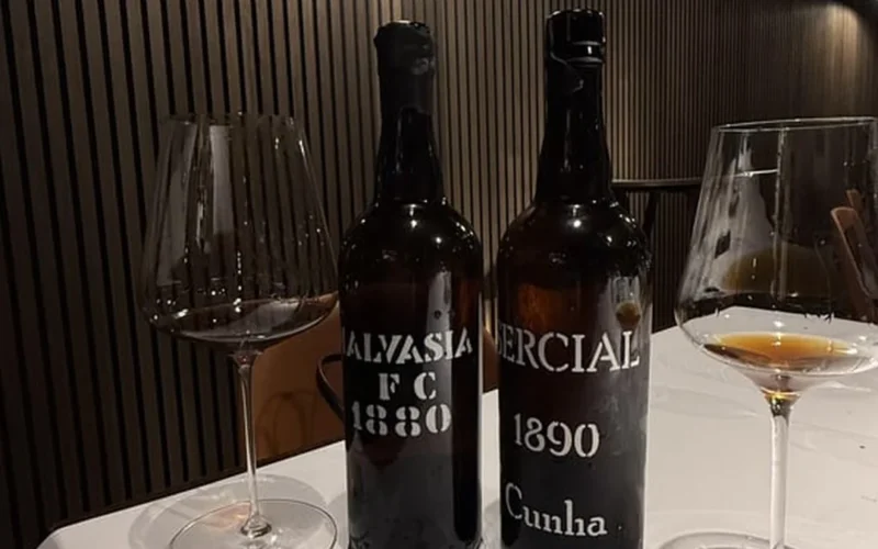 Aged Madeira wine bottle displayed on wooden surface with parchment, glowing under warm light.