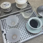 Sleek bar drip tray with ceramic mugs and tea leaves in minimalist bar setup under soft natural light.