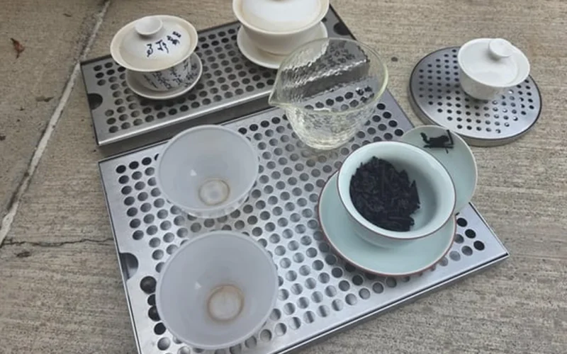 Sleek bar drip tray with ceramic mugs and tea leaves in minimalist bar setup under soft natural light.