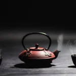 Dark tea leaves unfurling in a clay teapot with steam rising in a dimly lit room.