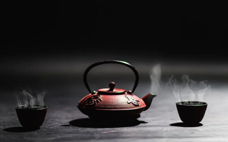 Dark tea leaves unfurling in a clay teapot with steam rising in a dimly lit room.