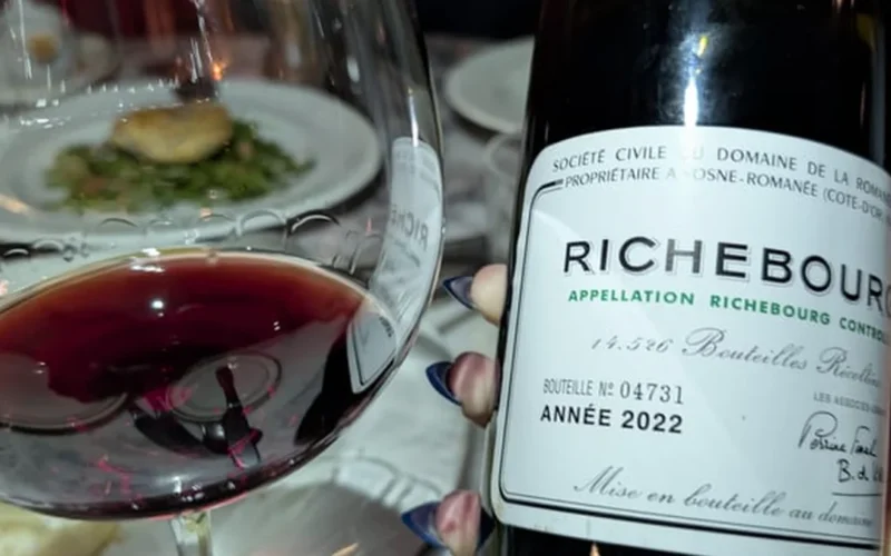 A dark red wine glass with swirling liquid under warm lighting next to wooden barrels.