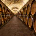 Aged wine bottle and barrel in a dimly lit cellar with warm golden lighting.