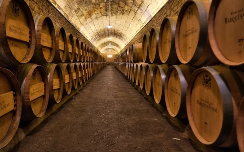 Aged wine bottle and barrel in a dimly lit cellar with warm golden lighting.