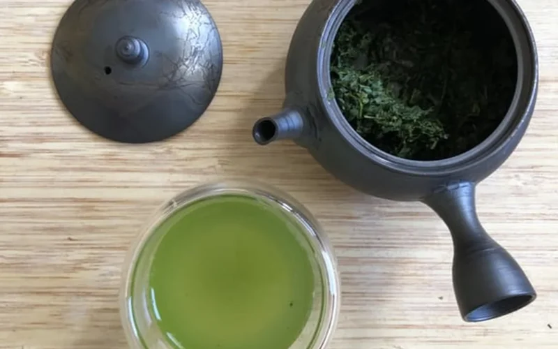 Porcelain bowl with green tea leaves unfurling, steam rising under soft light.
