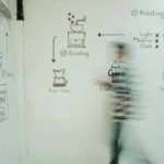 Dark coffee beans spilling from hot roaster with smoke rising under industrial lighting.