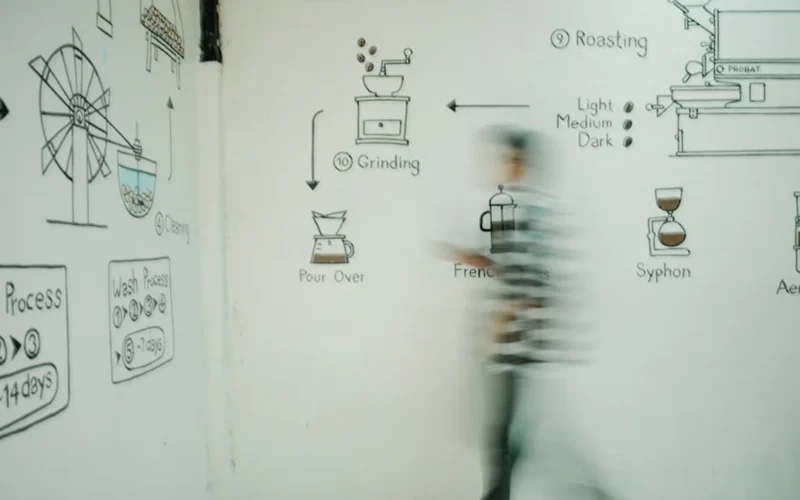 Dark coffee beans spilling from hot roaster with smoke rising under industrial lighting.