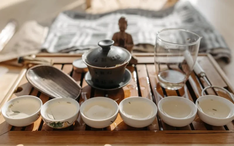 Gaiwan with Longjing Dragonwell tea, steam rising, wooden tray and bamboo strainer in soft morning light.