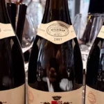 A dark aged wine bottle surrounded by wooden barrels and parchment notes under warm lighting.