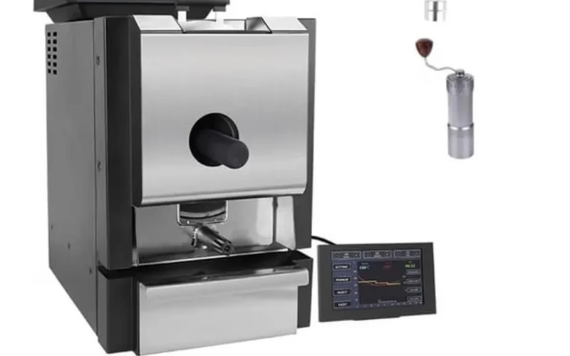 Black coffee roaster emitting steam in rustic kitchen setting with coffee beans and parchment nearby.