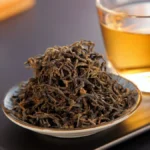 A close-up of aged puer tea leaves steaming in a clay teapot on a wooden table under warm light.