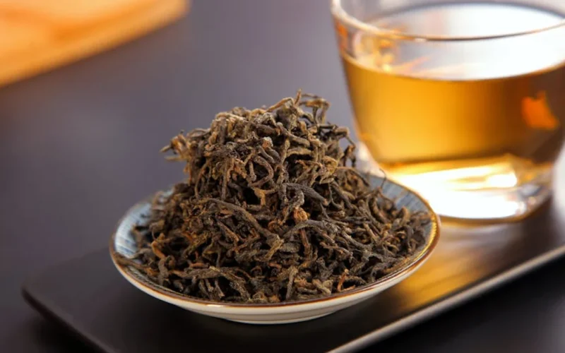 A close-up of aged puer tea leaves steaming in a clay teapot on a wooden table under warm light.