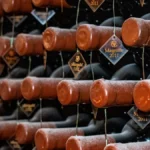 Aged wine bottle in vintage cellar setting with soft lighting and surrounding glassware and books.