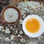 Aged puer tea cake on bamboo tray with scattered tea leaves under warm lighting.