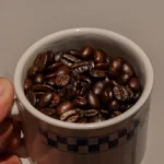 Dark roast coffee cup with beans and a digital screen displaying roast data under warm lighting.