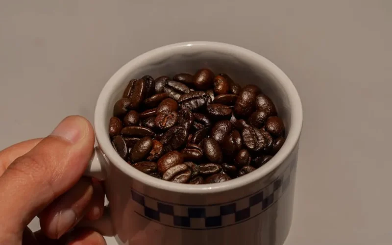 Dark roast coffee cup with beans and a digital screen displaying roast data under warm lighting.