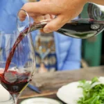 Golden Aligote wine pouring from decanter into glass with wine book nearby.