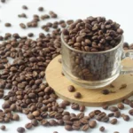 Dark roast coffee beans spilling from hand with golden light reflecting on their surface against wooden crates and dried