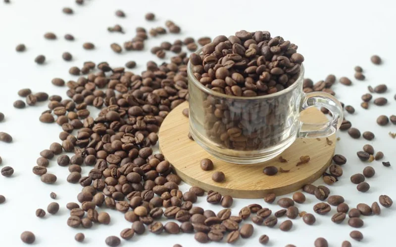 Dark roast coffee beans spilling from hand with golden light reflecting on their surface against wooden crates and dried