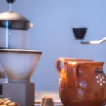 Traditional Yemeni coffee grinder in desert setting with rising aroma and clay pot nearby.