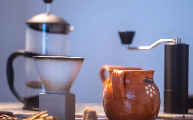 Traditional Yemeni coffee grinder in desert setting with rising aroma and clay pot nearby.