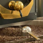 Coffee roaster showing first crack with steam rising in industrial kitchen setting.