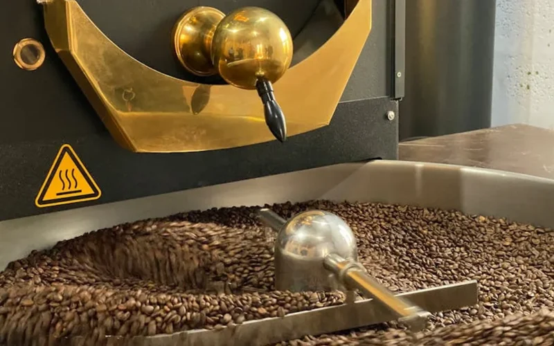 Coffee roaster showing first crack with steam rising in industrial kitchen setting.