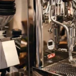 Two high-end espresso machines with steam and coffee grounds on a clean countertop under soft lighting.