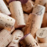 Aged wine bottle with cracked cork on wooden table emitting faint red fruit aroma in soft light.