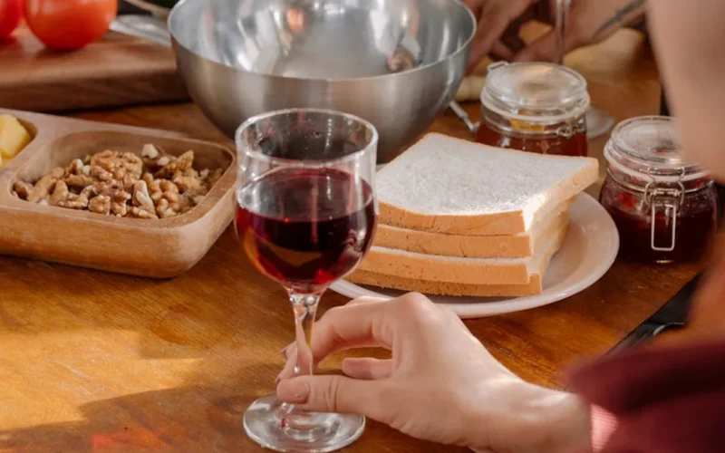 A deep red wine glass on a wooden table with dried herbs and a flickering candle flame.