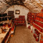 Organic Cava de Guarda Superior bottle in a rustic cellar with aged barrels and natural light.