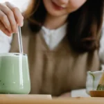 Pink cherry blossom petals floating in a frothy matcha latte with soft spring lighting.