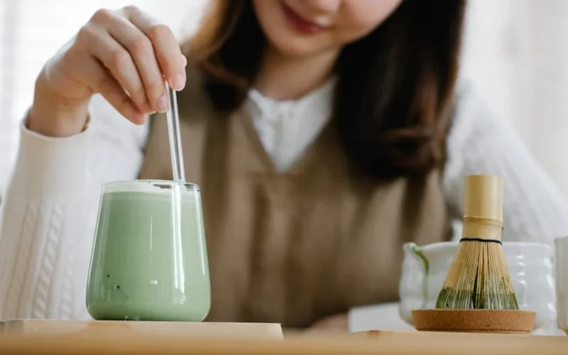 Pink cherry blossom petals floating in a frothy matcha latte with soft spring lighting.