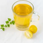 A steaming cup of jasmine green tea with white flowers floating in the liquid on a white background.
