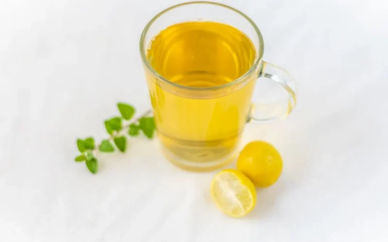 A steaming cup of jasmine green tea with white flowers floating in the liquid on a white background.