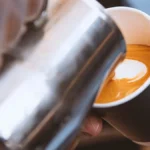 Barista creates heart latte art on frothy milk in a cozy coffee shop with single-origin beans and vintage espresso machi