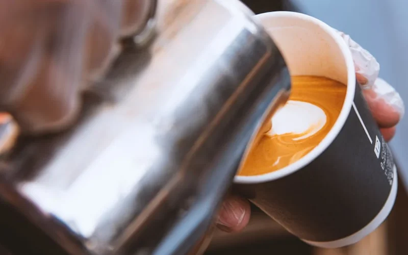 Barista creates heart latte art on frothy milk in a cozy coffee shop with single-origin beans and vintage espresso machi