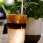 A colorful citrus slice with cold foam on iced coffee in a ceramic mug on a wooden table under natural light.