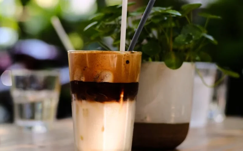A colorful citrus slice with cold foam on iced coffee in a ceramic mug on a wooden table under natural light.