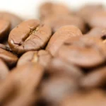 Hand using color meter to measure coffee beans during roasting process.