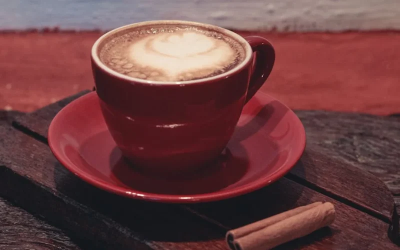 A steaming cortado coffee in a porcelain mug on a white counter with espresso machine and coffee bean.