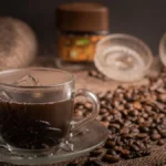 Coffee beans spilling from a roaster's bag onto a wooden table with steam and natural light.