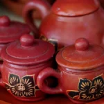 Dark tea leaves unfurling in a clay teapot with steam rising under warm golden light.