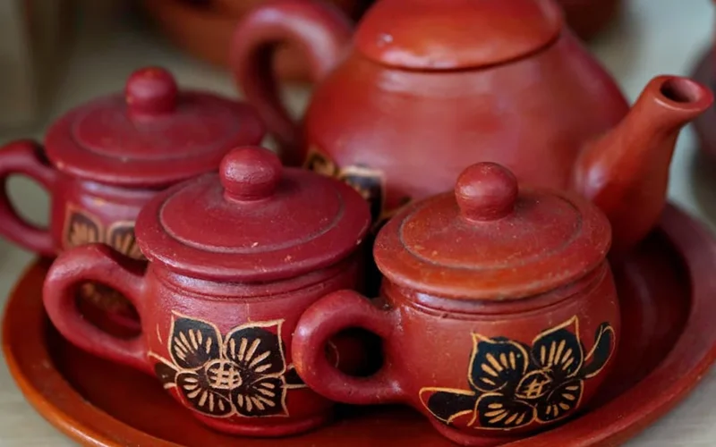 Dark tea leaves unfurling in a clay teapot with steam rising under warm golden light.