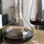 A dark red wine decanter surrounded by aged wood and leather under soft lighting.