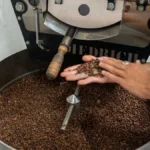 Electric roaster with coffee beans steaming under LED lighting in a modern coffee shop setting.
