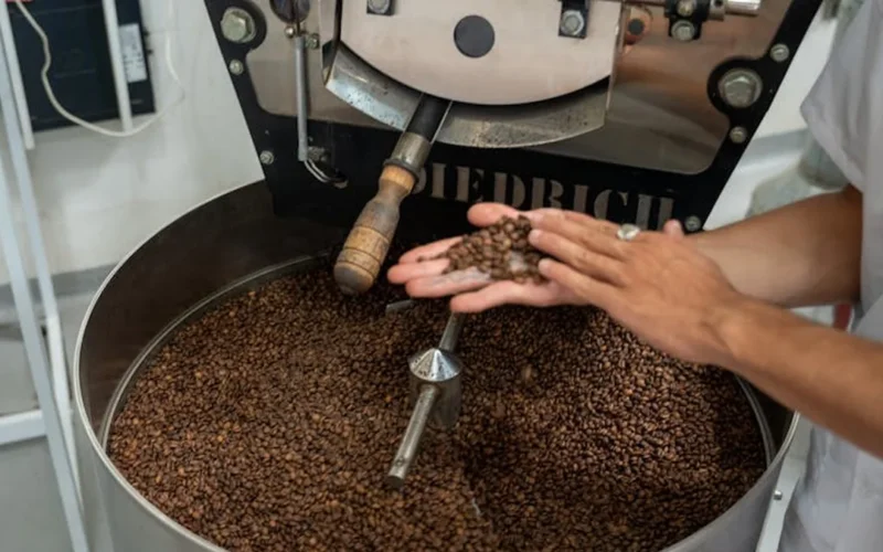 Electric roaster with coffee beans steaming under LED lighting in a modern coffee shop setting.