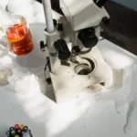 Scientific lab setup showing coffee between electrodes with LED lighting and steam rising.