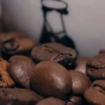A rich espresso shot in a copper cup with steam rising, dark roast beans and hand-painted mug on a wooden counter.